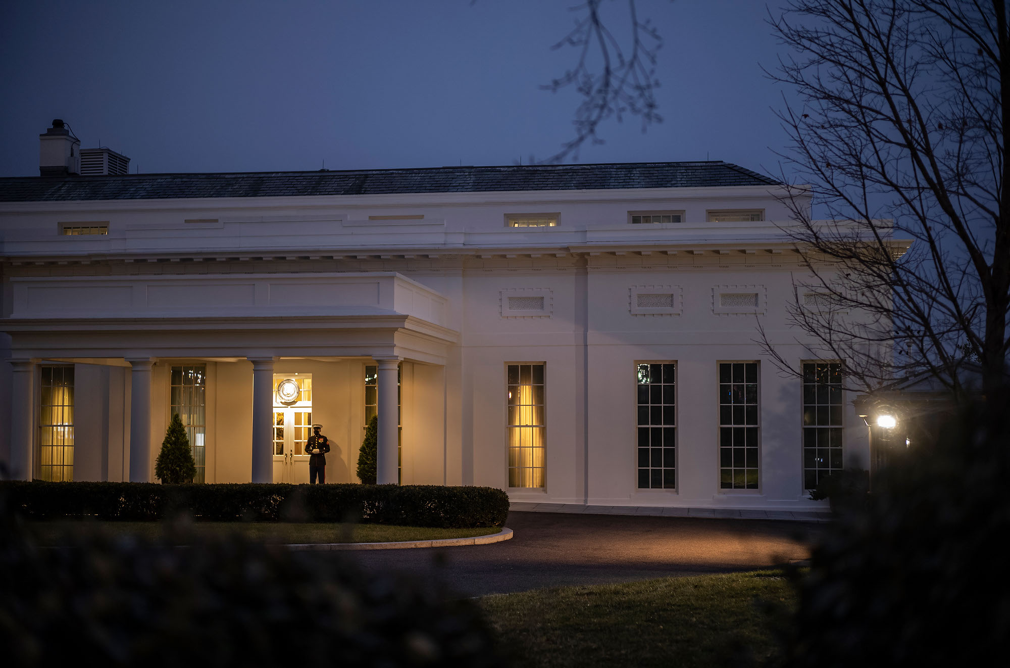 A Marine stands guard at the door to the West Wing of the White House indicating the presence of the president in that area. 