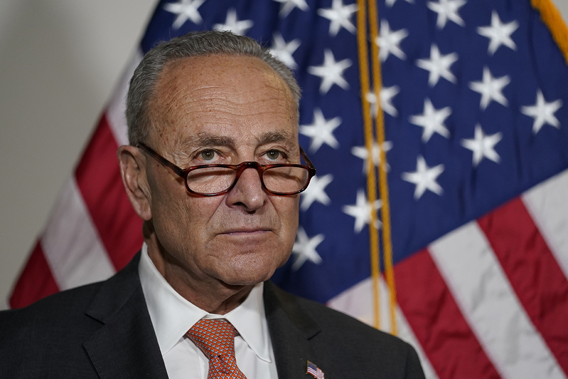 A close-up photo shows Chuck Schumer staring off-camera with American flags behind him during a press conference.