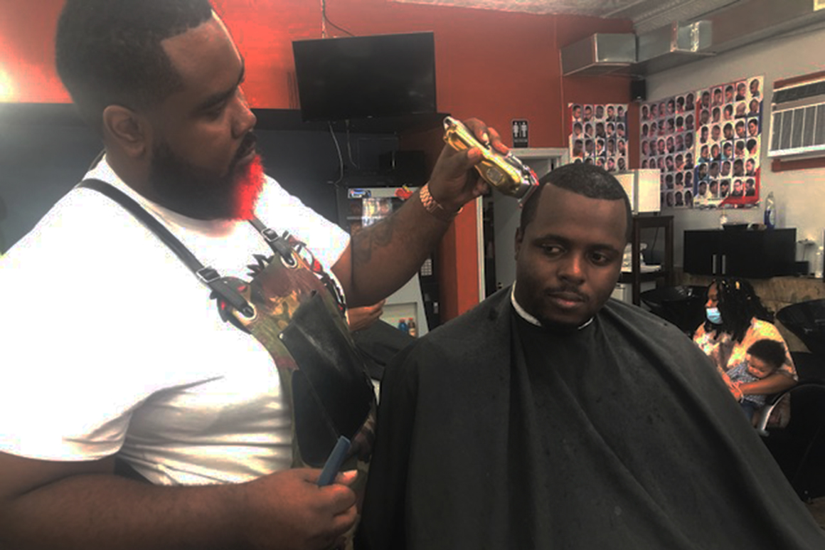 A barber passes his clippers over the head of a man seated in a barber chair.