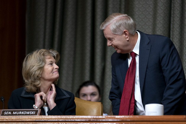 Sen. Lindsey Graham, right, stands while speaking to Sen. Lisa Murkowski, seated, during a Senate hearing.