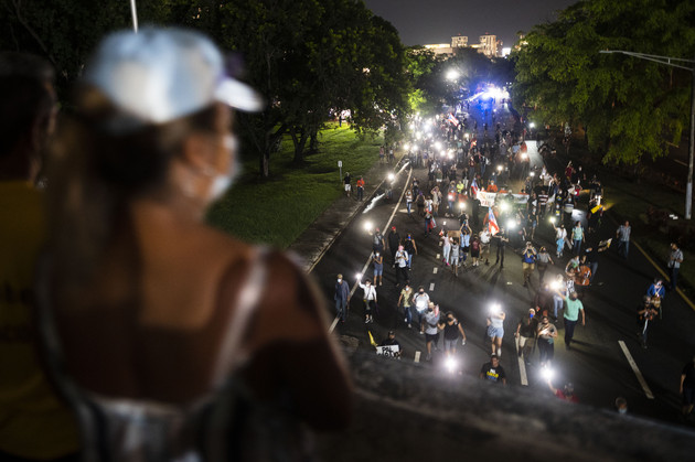A crowd of people march along Las Americas Highway at night with flashlights. 