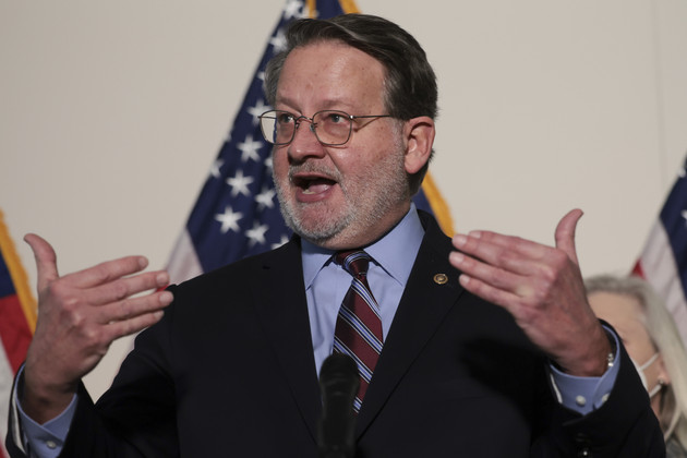 Sen. Gary Peters (D-Mich.) is shown speaking into a microphone at a press conference.