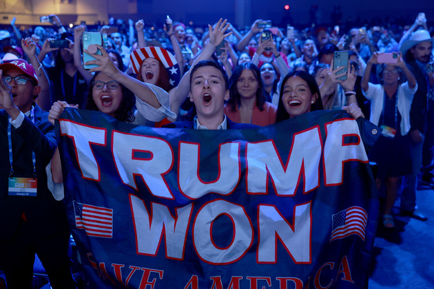 A person, standing in a crowd, holds a banner that partly reads &quot;TRUMP WON.&quot; 