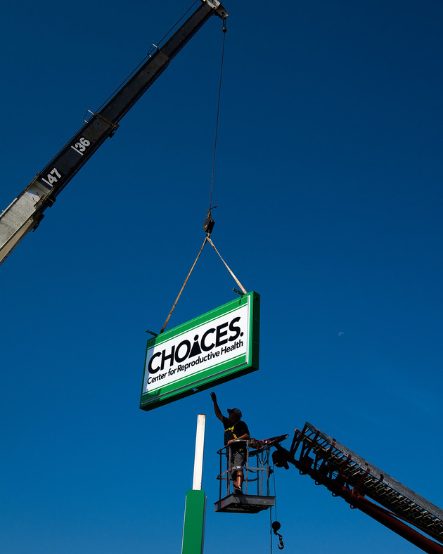 A person reaching to touch a green and white Choices sign as a crane holds it in the air.