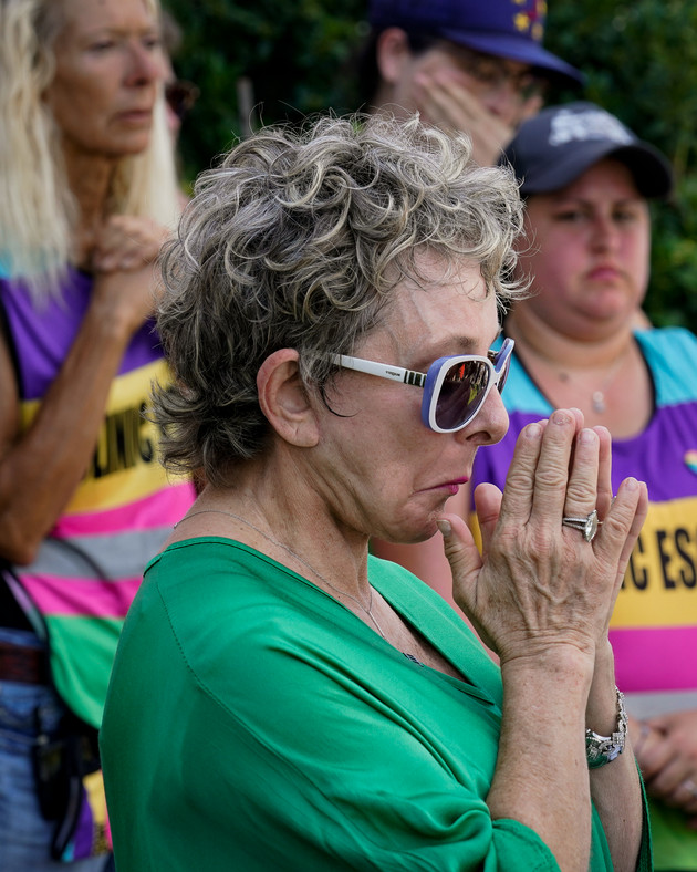 Diane Derzis standing with her hands in a prayer-like gesture, while abortion clinic escorts look on behind her.