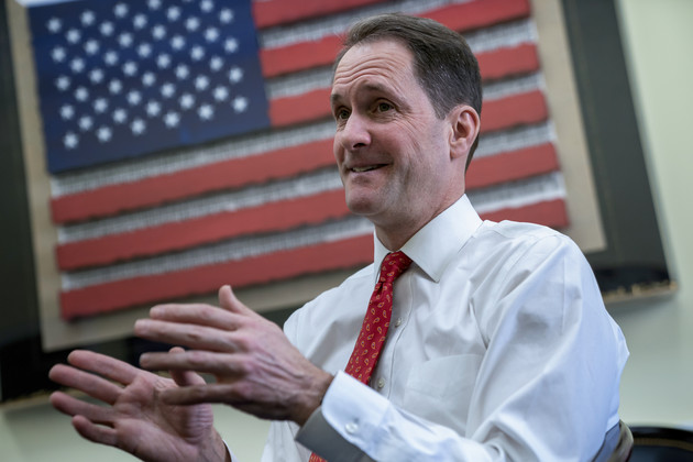 Representative Jim Himes speaking in front of a framed image of an American flag.