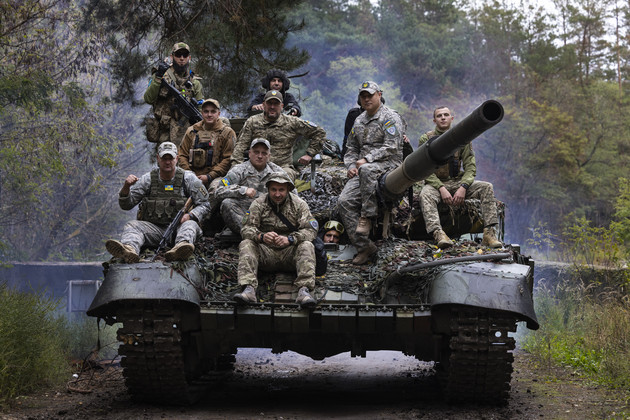 Ukrainian troops ride upon a repaired Russian tank in a wooded area.