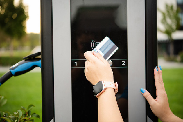 A person pays with a credit card at an electric vehicle charging station.