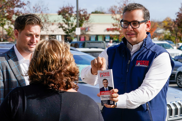 George Santos holding out a campaign pamphlet while speaking with a voter.