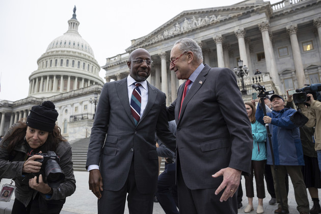 Sen. Raphael Warnock is greeted by Senate Majority Leader Chuck Schumer outside the U.S. Capitol as press stand behind the pair with cameras.
