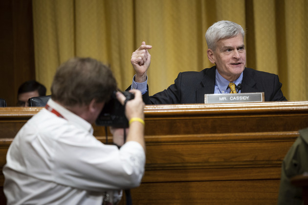 Sen. Bill Cassidy speaks behind a placard of his name as a photographer shoots him during a Senate hearing.