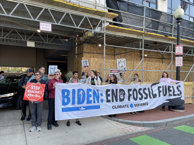 Protesters on a sidewalk hold signs that say &quot;Biden: End Fossil Fuels&quot; and &quot;Stop Manchin's #DirtyDeal&quot;