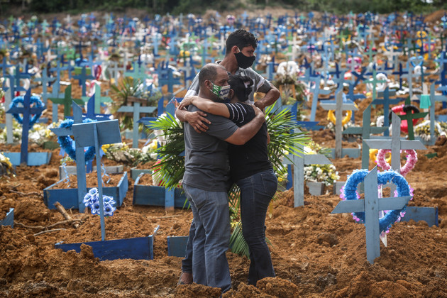  Relatives of a deceased person wearing protective masks mourn during a mass burial of coronavirus pandemic victims.