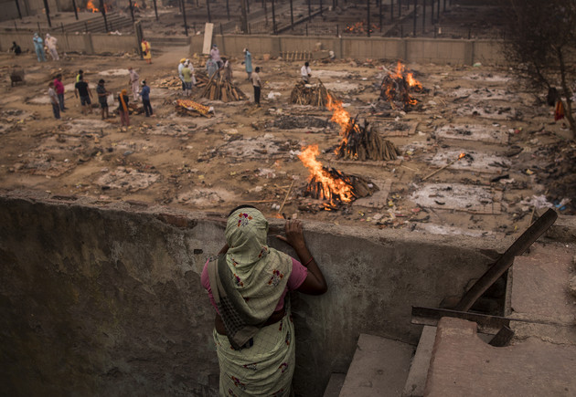 NEW DELHI, INDIA - MAY 09: A lady looks at the burning funeral pyres of the patients who died of the Covid-19 coronavirus from her house near a makeshift crematorium on May 09, 2021 in New Delhi, India. India broke a fresh record on Thursday with over 412,000 new cases of Covid-19 as the total number of those infected according to Health Ministry data neared 20 million. The real figure could be up to ten times higher, many health experts say, due to a lack of widespread testing or reporting, and only patients who succumbed in hospitals being counted. Hospitals have begun turning away people suffering from Covid-19, having run out of space for the crushing number of people seeking help. (Photo by Anindito Mukherjee/Getty Images)